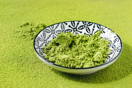 Green tea matcha powder in ceramic bowl over powdering matcha as background. Close upの写真素材