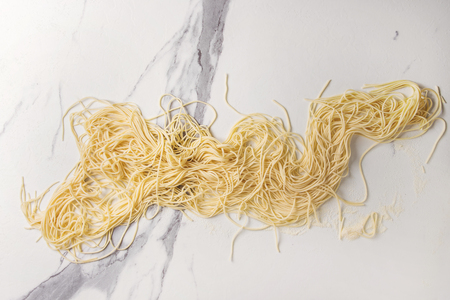 Homemade italian uncooked pasta spaghetti with semolina flour over white marble texture background. Flat lay, space.の写真素材
