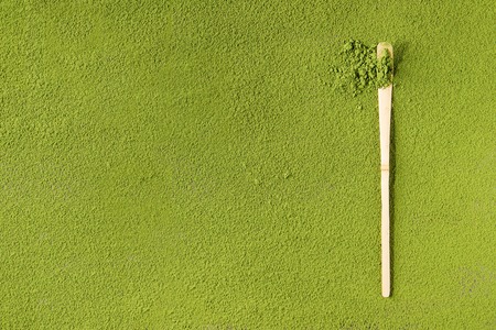 Green tea matcha powder in traditional bamboo spoon over powdering matcha as background.の写真素材