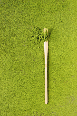 Green tea matcha powder in traditional bamboo spoon over powdering matcha as background.の写真素材