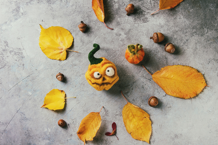 Funny craft Halloween needle felted pumpkins jack o lantern holiday decor with autumn yellow leaves and acorns over grey texture background. Flat lay, copy spaceの写真素材