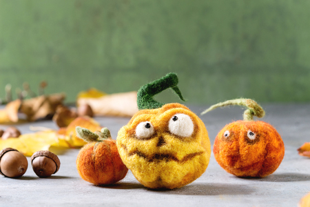 Funny craft Halloween needle felted pumpkin jack o lantern holiday decor with autumn yellow leaves and acorns over grey texture background.の写真素材
