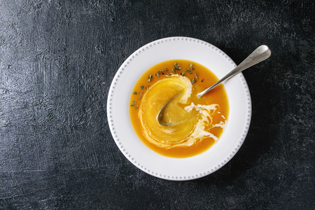 Plate of vegetarian pumpkin carrot soup decorated by herbs and cream, with spoon inside over black texture background. Flat lay, copy spaceの写真素材