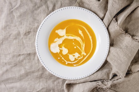 Plate of vegetarian pumpkin carrot soup decorated by cream spots over linen cloth as background. Flat lay, copy spaceの写真素材