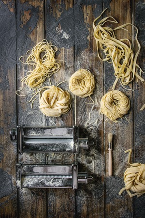 Variety of italian homemade raw uncooked pasta spaghetti and tagliatelle with pasta maker rolled machine and semolina flour over dark plank texture wooden table. Flat lay, spaceの写真素材