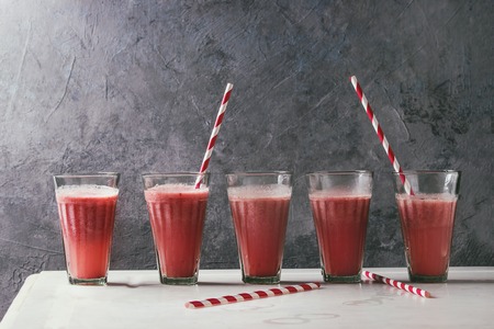 Red fruit berries watermelon iced cocktail in glasses in row with striped straw stand on white...