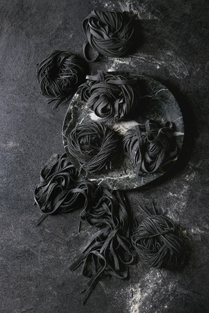 Variety of italian homemade raw uncooked cuttlefish ink black pasta spaghetti and tagliatelle with semolina flour over black texture background. Flat lay, space.の写真素材