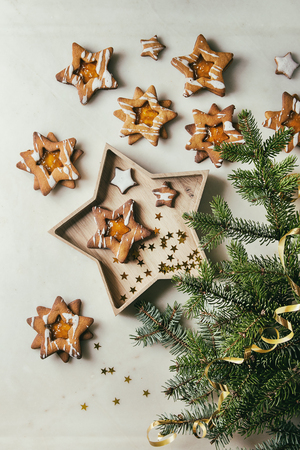 Homemade Christmas star shape sugar caramel cookies with frosting and orange citrus jam in wooden plate over white marble background with fir branches. Flat lay, space. Sweet xmas or new year gift.の写真素材