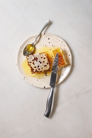 Organic honey in honeycombs with spoon and knife in spotted ceramic plate on white marble...