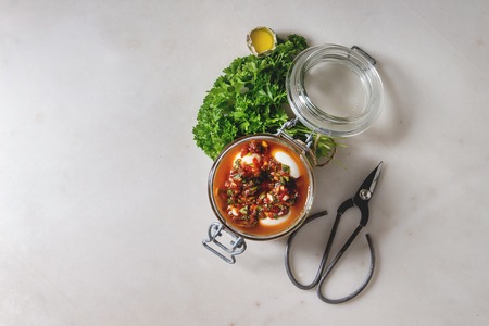 Opened Jar with homemade pickled marinated quail eggs in tomato and olive oil sauce with anchovies and fresh parsley on white marble background. Ingredients above. Flat lay, spaceの写真素材