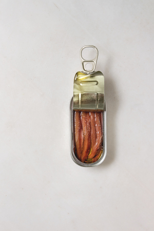 Pickled salted anchovies fillet in oil in open tin can over white marble background. Flat lay, copy spaceの写真素材