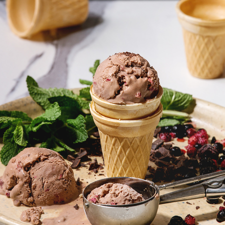 Homemade chocolate raspberry ice cream in small waffle cup served with frozen berries, fresh mint,...
