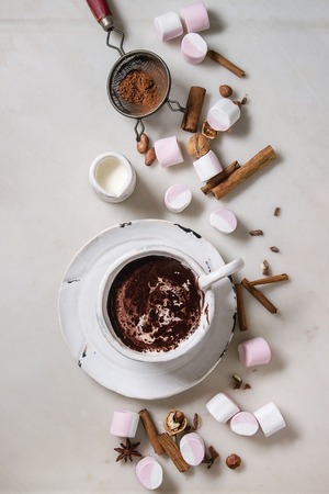 Ceramic cup of hot chocolate with marshmallow s'mores with ingredients above over white marble table. Winter drink. Flat lay, spaceの写真素材