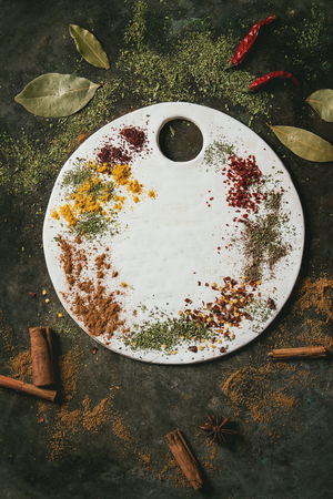 Spices seasoning and herbs variety. Red hot chili chili pepper, bay leaf, cinnamon powder and sticks, white ceramic board over dark metal background. Flat lay, space. Cooking conceptの写真素材