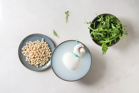 Bowl with whole tied Italian cheese burrata in brine, arugula salad and pine nuts over white marble background. Flat lay, spaceの写真素材