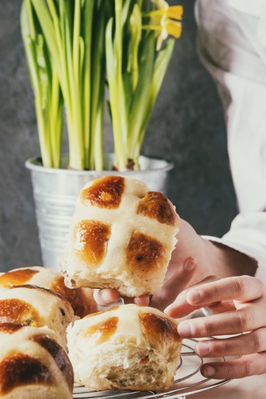 Child hands take homemade Easter traditional hot cross buns on cooling rack on white marble table...