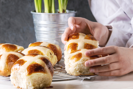 Child hands take homemade Easter traditional hot cross buns on cooling rack on white marble table with narcissus flowers.の写真素材