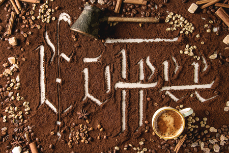 Calligraphic inscription gothic letters coffee over ground black coffee scattered on white marble with roasted and unroasted beans, pot, cup of espresso. Coffee drinking concept background. Top viewの写真素材