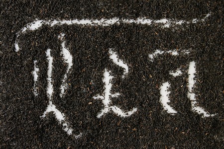 Calligraphic inscription gothic letters tea over dry black ceylon tea scattered on white marble. Tea drinking concept background. Top viewの写真素材