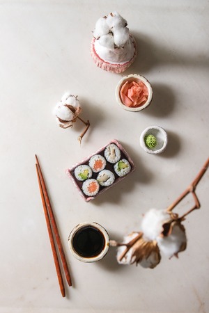 Sushi rolls set in pink ceramic serving plate with chopsticks, bowls of soy sauce, and pickled ginger, cotton flowers over white marble background. Flat lay, space. Japan menuの写真素材