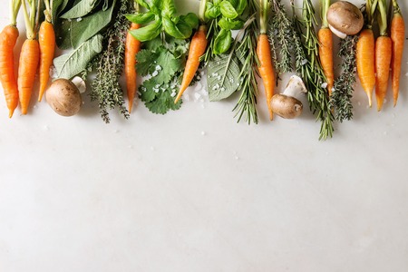 Variety of fresh kitchen herbs with mini carrots and champignon mushrooms in row over white marble background. Flat lay, space. Cooking concept, food background.の写真素材