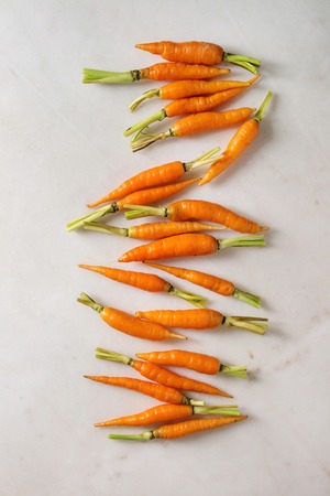 Young mini carrot in row over white marble background. Flat lay, space. Cooking concept, food...