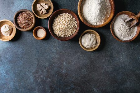 Ingredients for baking bread. Variety of wheat and rye flour, grains, yeast, sourdough over dark blue texture background. Flat lay, spaceの写真素材