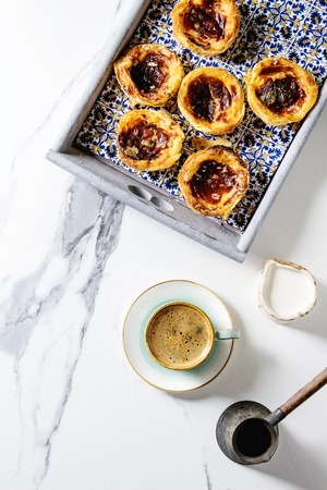 Traditional Portuguese egg tart dessert Pasteis Pastel de nata in classic tile tray with cup of black coffee and jug of milk over white marble background. Flat lay, spaceの写真素材