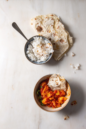 Started eaten Vegan vegetarian curry with ripe yellow jackfruit served in ceramic bowl with rice, coriander and homemade flatbread flapjack over white marble background. Flat lay, spaceの写真素材