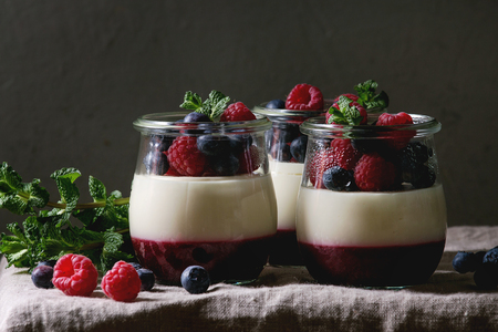 Homemade classic dessert Panna cotta with raspberry and blueberry berries and jelly in jars, decorated by mint leaves over linen table cloth with grey wall at background.の写真素材