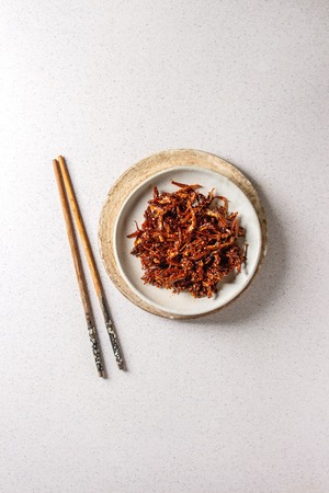 Vietnamese traditional hot spicy anchovies fish snack in ceramic plates with chopsticks over grey spotted background. Flat lay, space.の写真素材