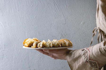 Fried asian dumplings Gyozas potstickers on white ceramic tray in female hands. Grey wall at...