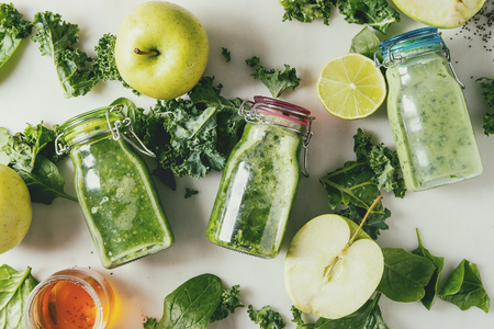 Variaty of green spinach kale apple honey smoothies in glass bottles with ingredients above over white marble background. Healthy organic eating. Flat lay, spaceの写真素材
