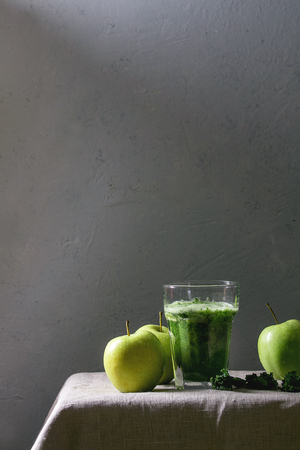 Green spinach kale apple smoothie in glass on linen table cloth with ingredients above. Healthy organic eating.の写真素材