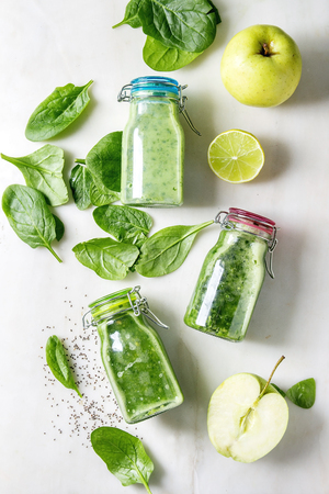 Variaty of green spinach kale apple smoothies in glass bottles with ingredients above over white marble background. Healthy organic eating. Flat lay, spaceの写真素材