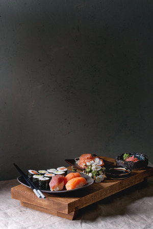 Sushi Set nigiri and sushi rolls on japanese wooden serving board with soy sauce, chopsticks, spring blossom cherry branches on grey linen table cloth. Japan menuの写真素材