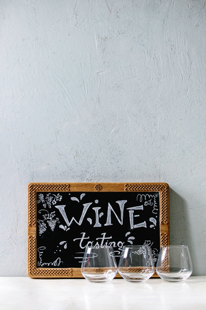 Wine tasting concept. Three empty old fashion wine glasses and decorative chalkboard with handwritten chalk lettering Wine tasting on white marble table. Copy spaceの写真素材