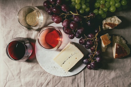 Variety of wine. Red, rose and white wine in old fashion glasses with bunches of grapes, blue cheese on ceramic board and bread on grey linen cloth. Dark still life. Flat lay, spaceの写真素材