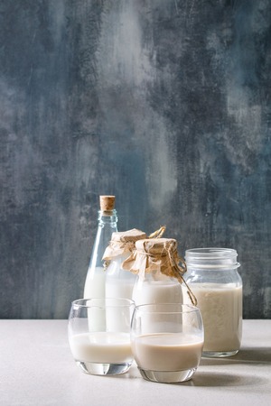 Variety of non-dairy vegan lactose free nuts and grain milk almond, hazelnut, coconut, rice, oat in glass bottles on white table with blue background.の写真素材