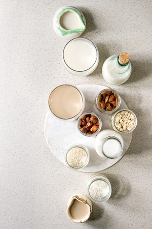Variety of non-dairy vegan lactose free nuts and grain milk almond, hazelnut, coconut, rice, oat in glass bottles and ceramic jugs with ingredients above over white spotted background. Flat lay, spaceの写真素材