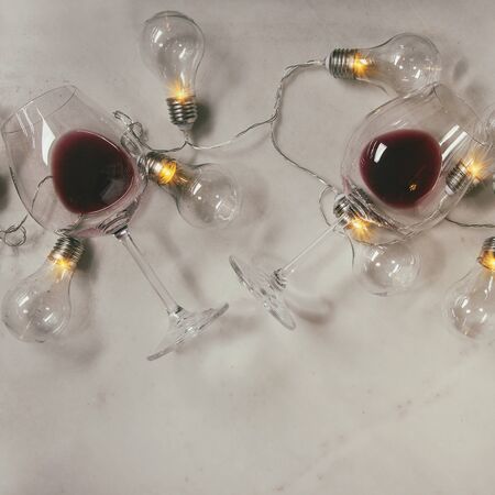 Two glasses of red wine and retro christmas garland with lighted lamps over white marble background....