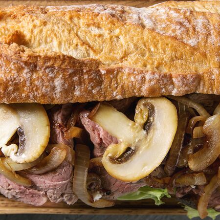 Close up of beef baguette sandwich with champignon mushrooms, green salad, fried onion. Top view, close up. Square imageの写真素材