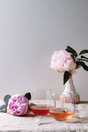 Two glasses of different rose wine standing on grey linen table cloth with pink peonies flowers. Romantic greeting card. Copy spaceの写真素材