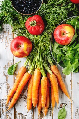Variety of fresh fruits, vegetables and berries carrot, spinach, tomatoes, red apples, blueberries over white plank wooden background. Flat lay, spaceの写真素材