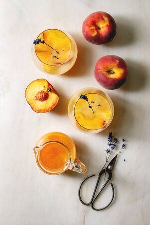 Peach cold lemonade or Bellini cocktail with lavender flowers served in two glasses with pitcher of pesh juice over white marble background. Flat lay, space. Homemade summer drink.の写真素材