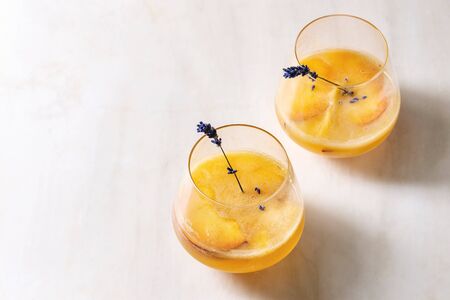 Peach cold lemonade or Bellini cocktail with lavender flowers served in two glasses on white marble table. Homemade summer drink. Copy spaceの写真素材