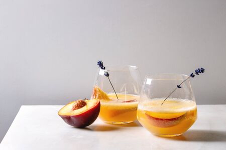 Peach cold lemonade or Bellini cocktail with lavender flowers served in two glasses on white marble table. Homemade summer drink. Copy spaceの写真素材