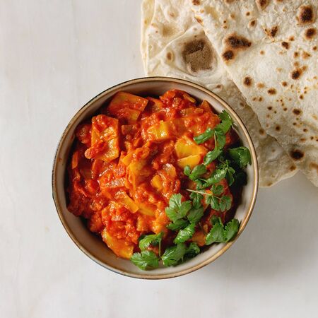 Vegan vegetarian curry with ripe yellow jackfruit served in ceramic bowl with coriander and homemade flatbread flapjack over white marble background. Flat lay, space. Square imageの写真素材