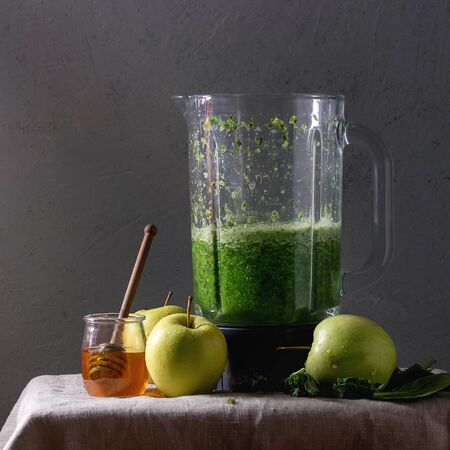 Green spinach kale apple honey smoothie in glass blender on linen table cloth with ingredients above. Healthy organic eating. Square imageの写真素材