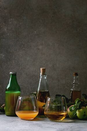 Variety of apple drinks. Bottles ang glasses of apple juice, vinegar and cider with garden apples with leaves and branches on table with dark background. Autumn home harvesting.の写真素材